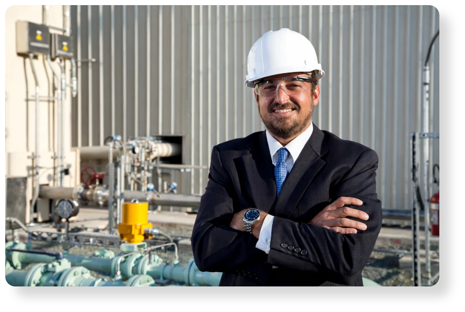 Confident industrial professional wearing a hard hat and safety glasses, standing with folded arms in a modern processing facility.