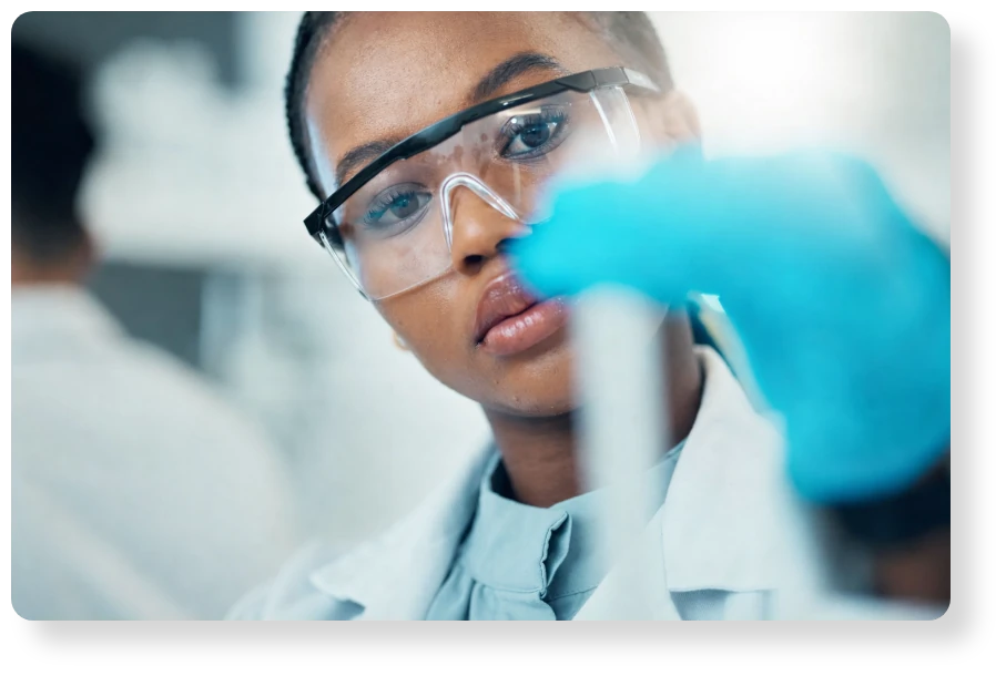 Close-up of a scientist wearing protective glasses and gloves while carefully examining laboratory equipment.