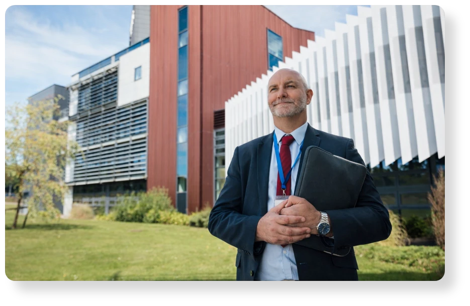 Business professional in a suit holding a portfolio outside a modern office building.