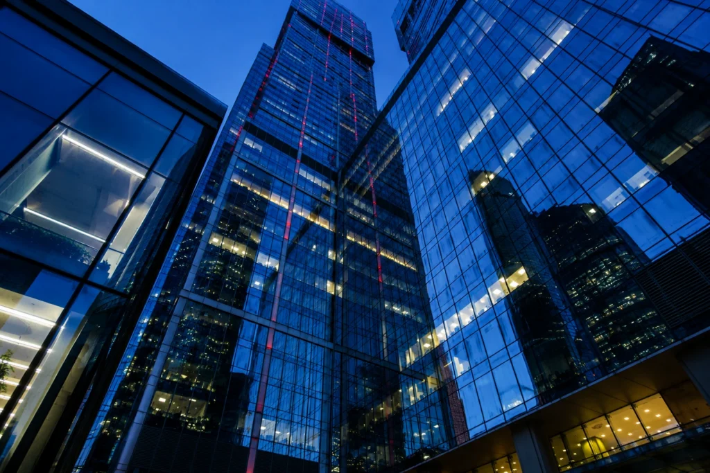 Modern glass office towers and corporate buildings illuminated at dusk, viewed from below in a contemporary business district.