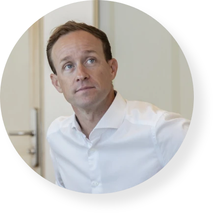Professional in a white shirt seated in an office, looking thoughtfully to one side.